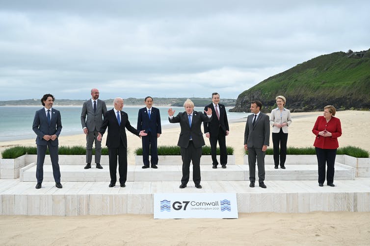 Boris Johnson está de pie con los brazos en alto frente a otros líderes del G7 en una playa.