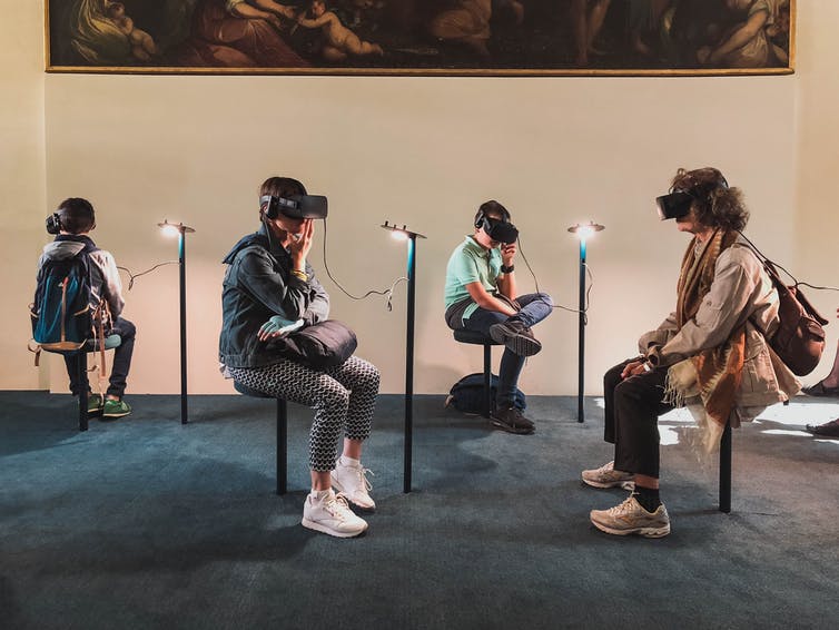 Cuatro personas con cascos de realidad virtual encaramados en taburetes