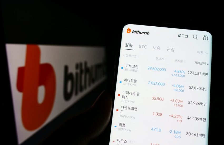 A cellphone displays the app of the South Korean crypto exchange Bithumb on its screen, with the exchange’s logo visible in the background.