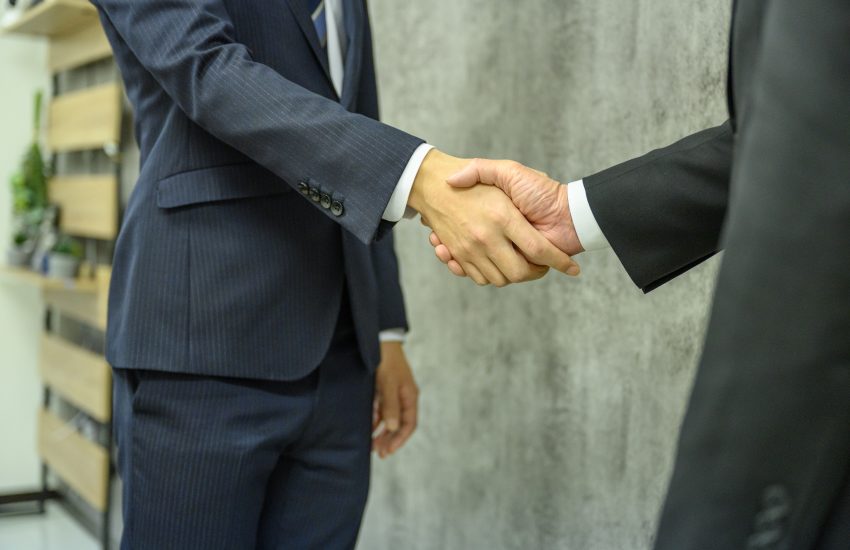 Two people dressed in suits shake hands.