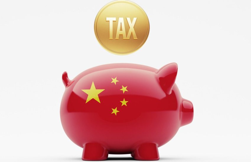 A golden coin with the word “tax” on it hangs above a piggy bank decorated in the colors of the Chinese flag.