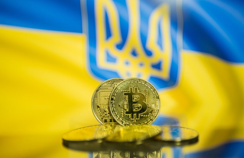 Five metal coins decorated with the Bitcoin logo against the backdrop of a Ukrainian flag, featuring the trident-style national symbol.