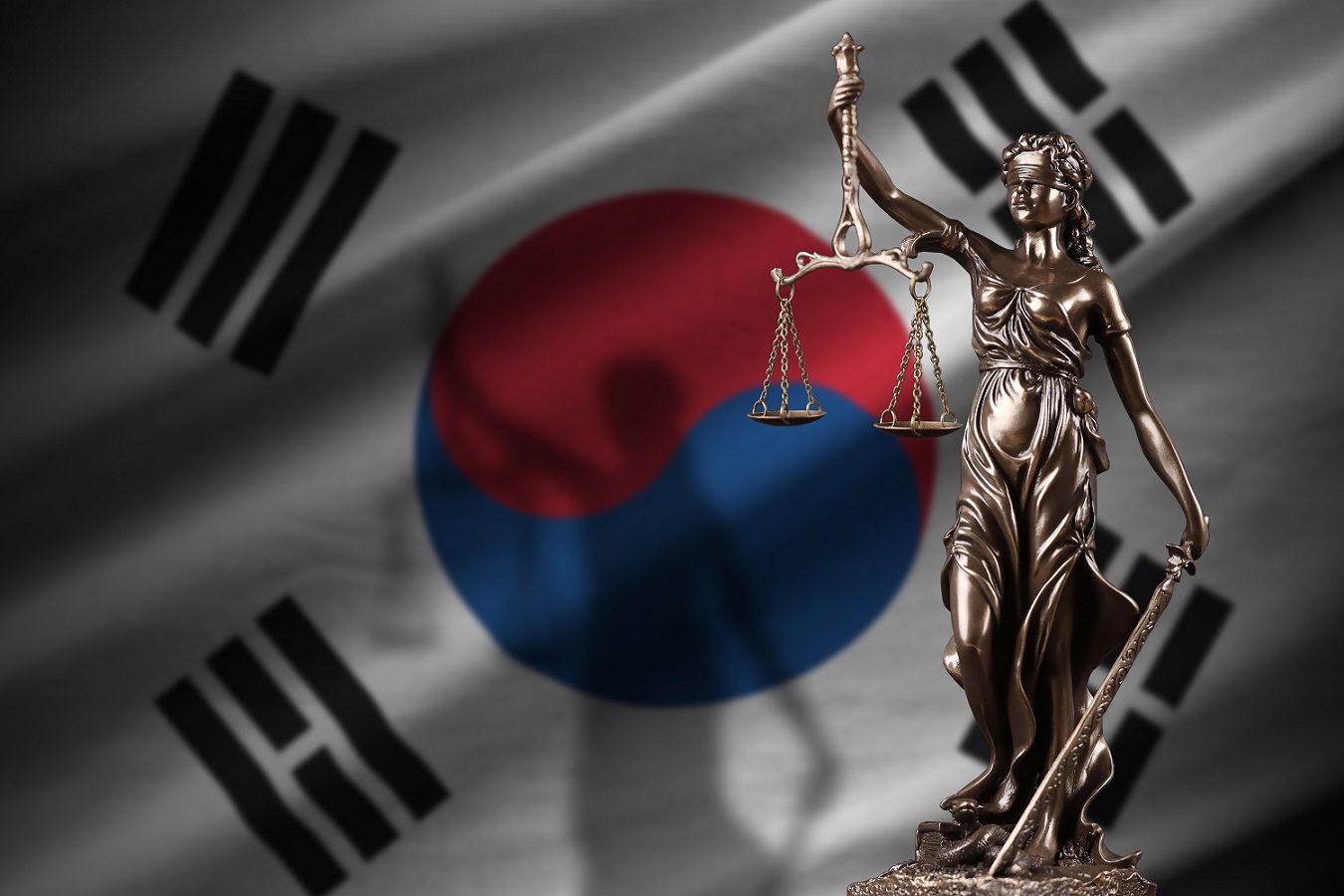 Una estatua de Lady Justice, con los ojos vendados y sosteniendo una balanza y una espada, frente a una bandera de Corea del Sur.
