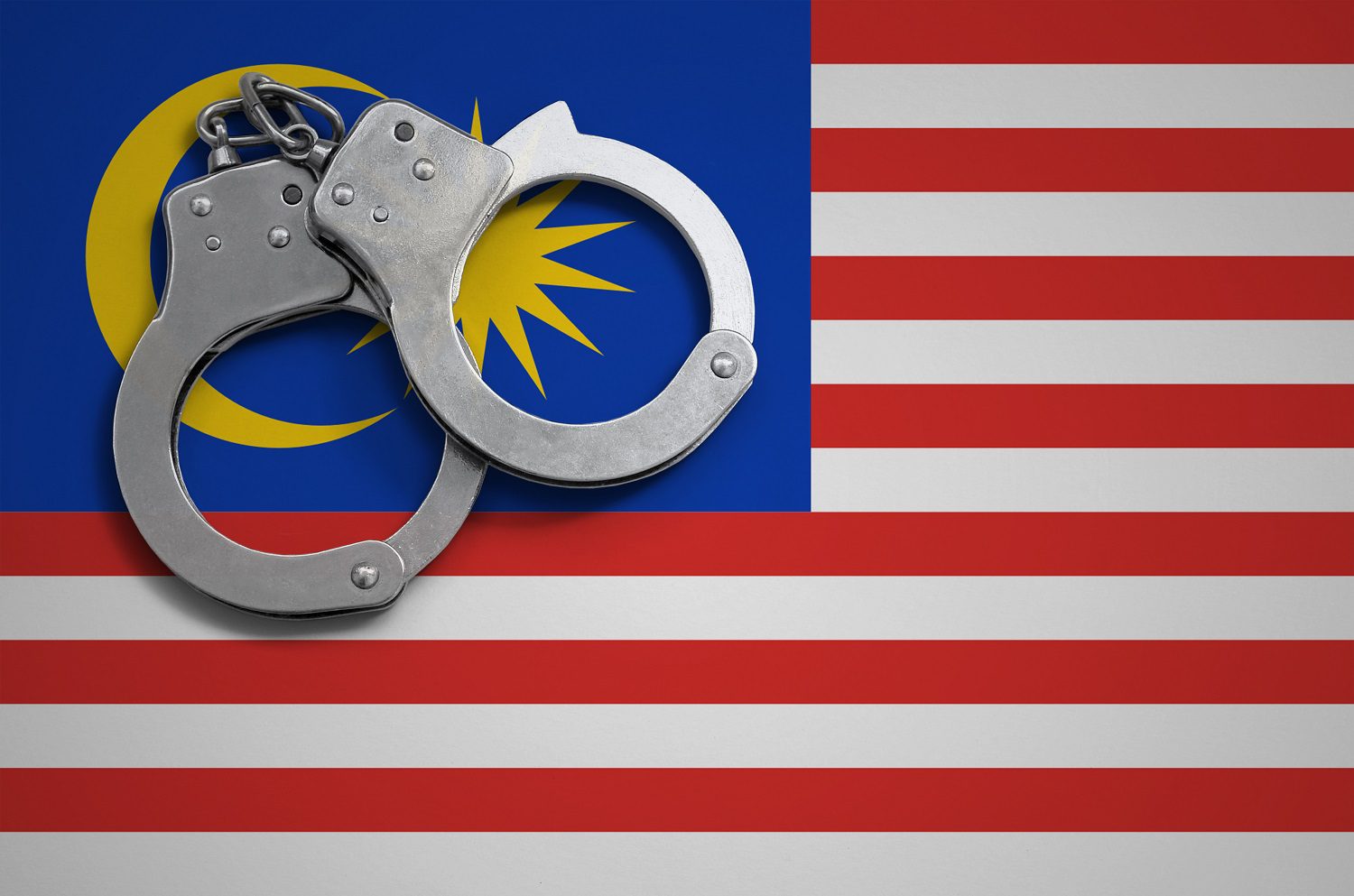 Un par de esposas policiales descansan sobre la bandera de Malasia.