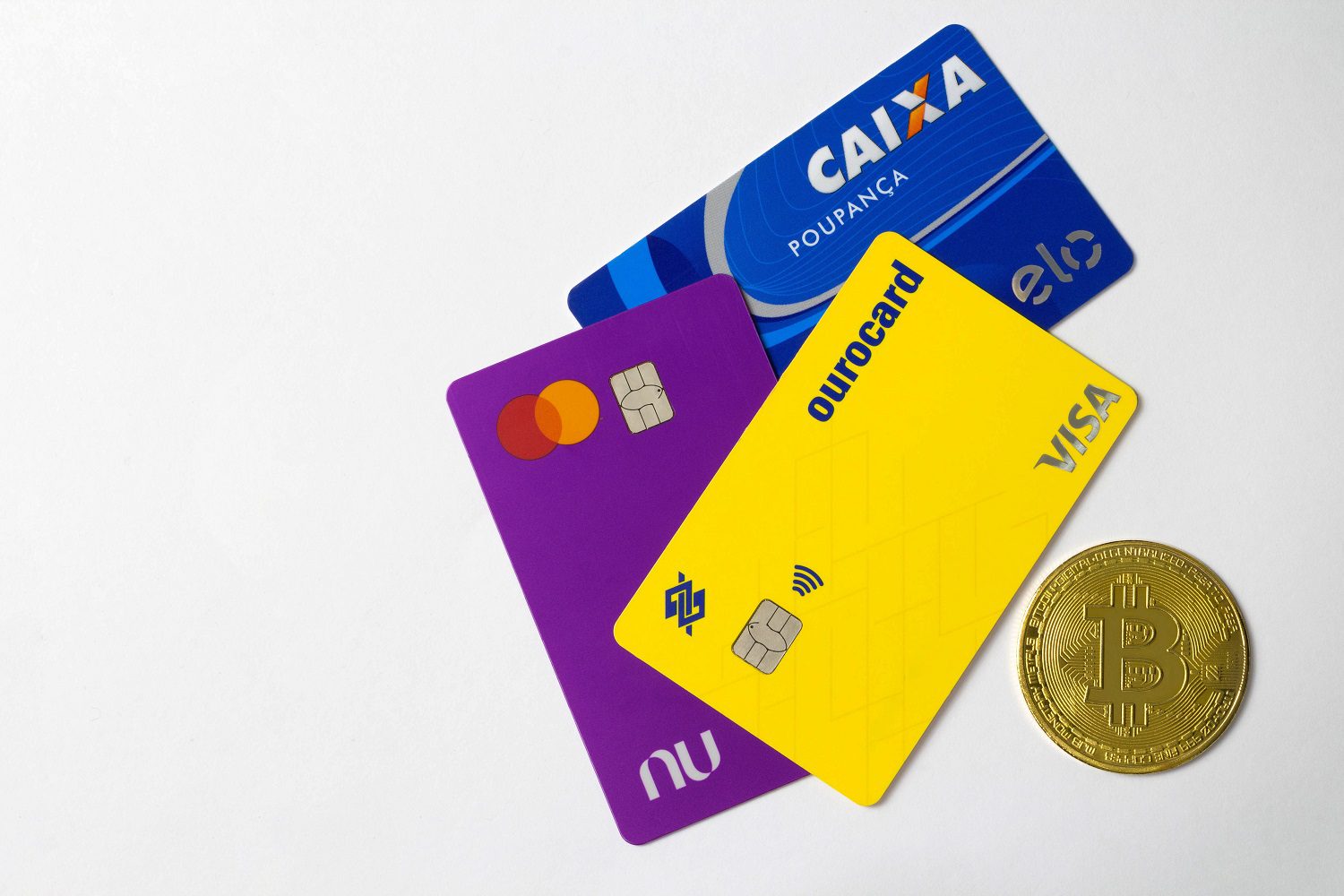Tres tarjetas bancarias brasileñas junto a una moneda de metal destinada a representar Bitcoin.