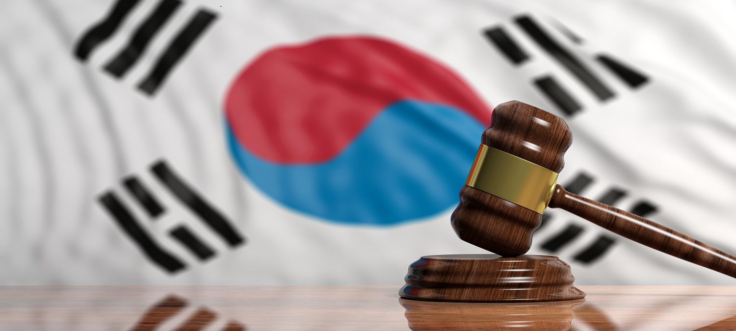 El mazo y el bloque de un juez sobre una mesa con la bandera de Corea del Sur al fondo.