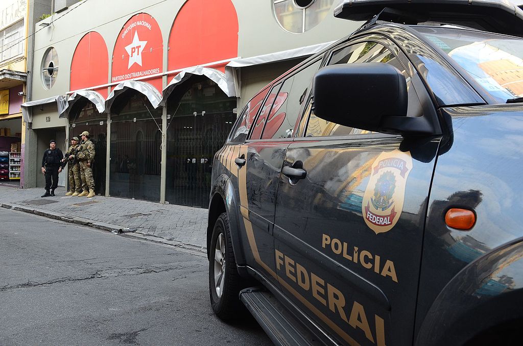 Oficiales armados de la policía y el ejército brasileños se paran afuera de un edificio con un vehículo policial en primer plano.
