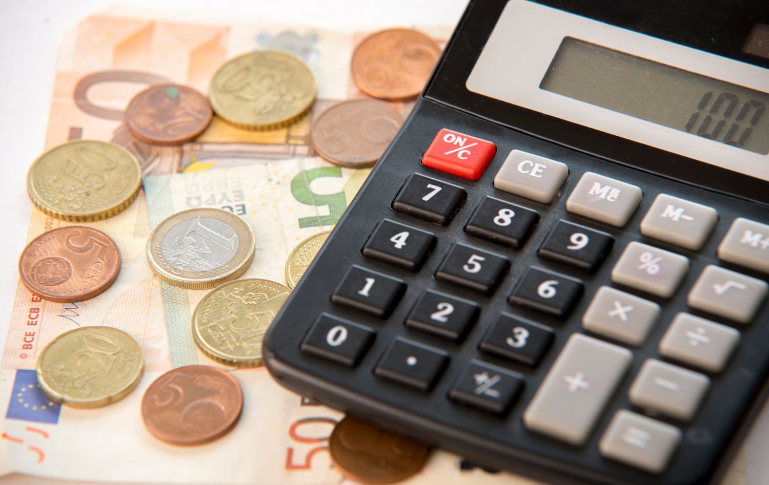 Una calculadora descansa sobre una pila de billetes en euros y junto a monedas de la misma moneda.