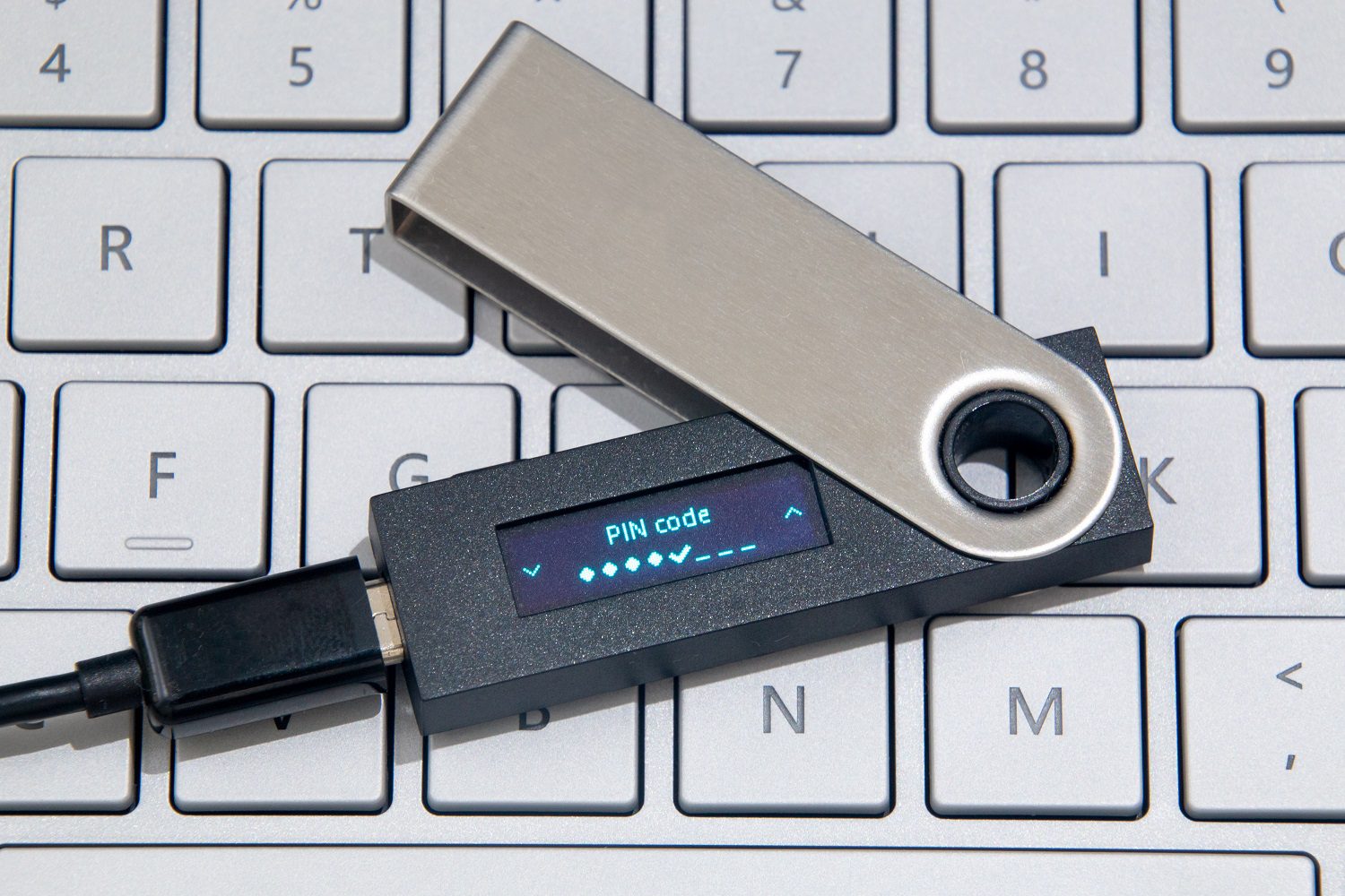 Una billetera de hardware criptográfico, conectada a un cable a través de una toma USB, descansa sobre el teclado de una computadora portátil.