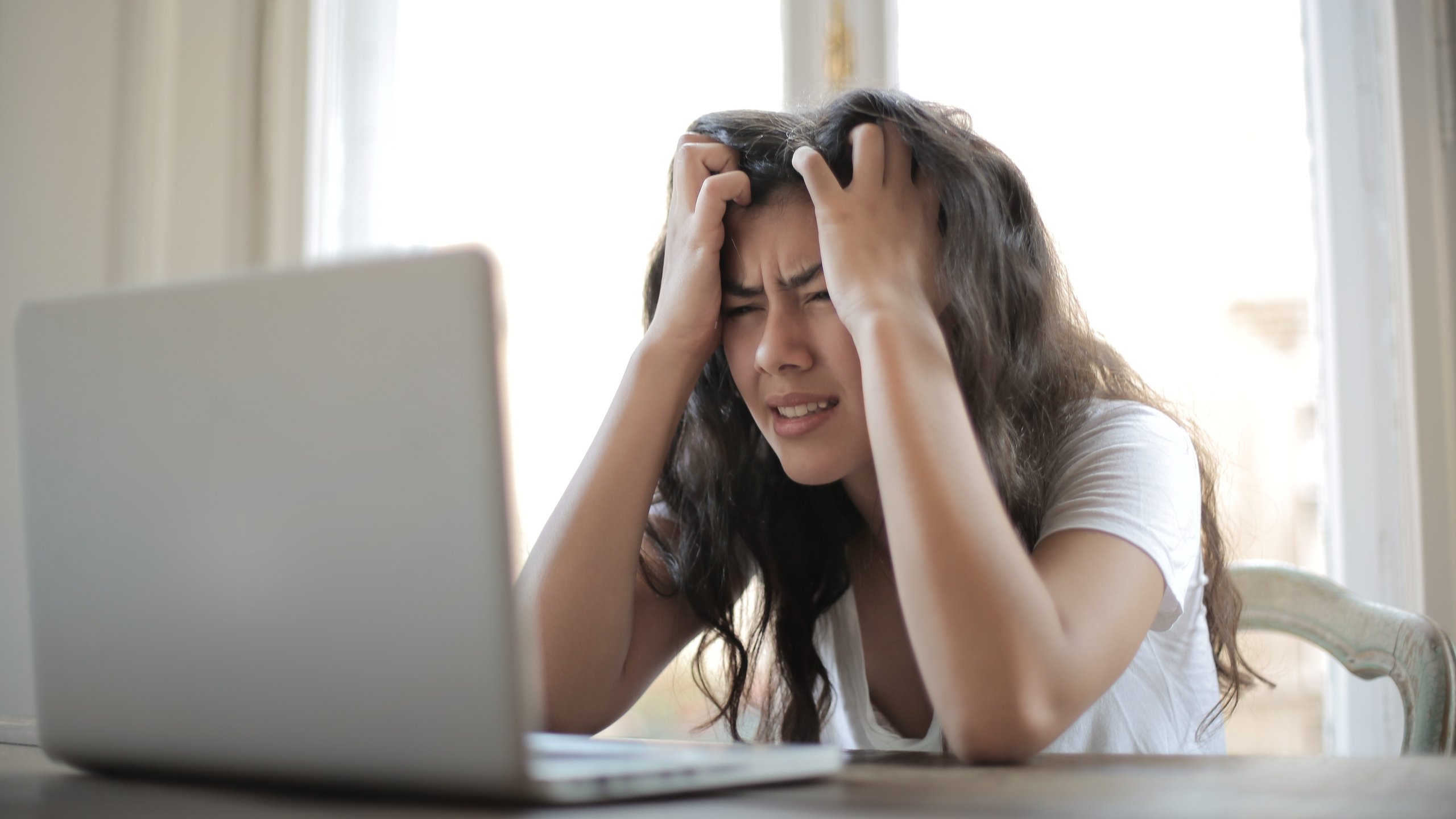 A woman is holding her head in front of her laptop.