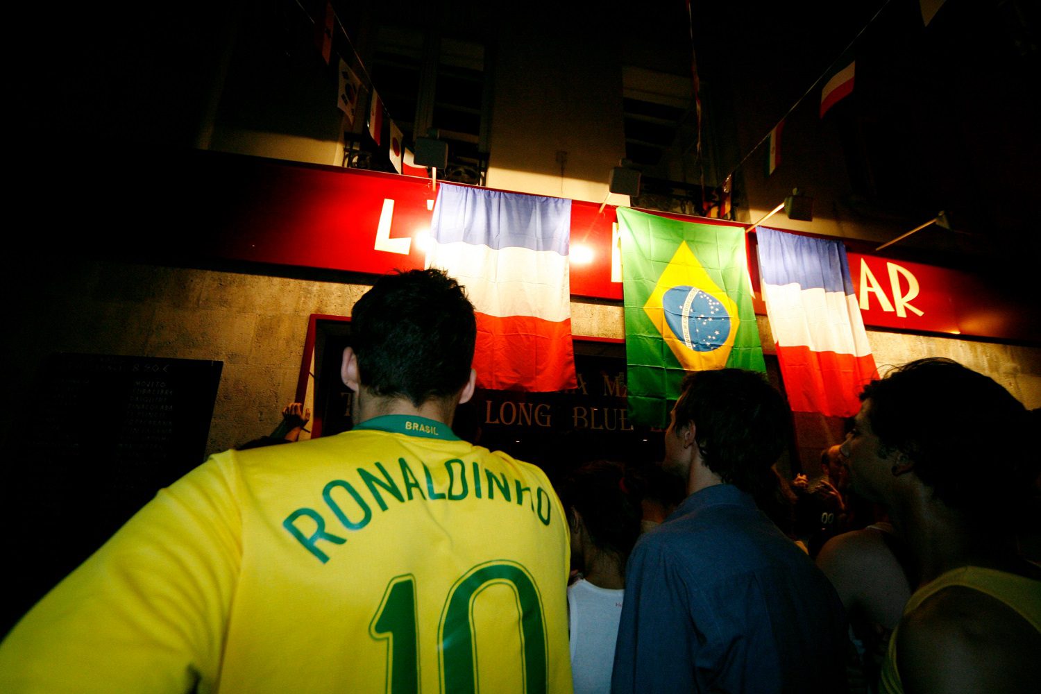 El fútbol (aficionados al fútbol) se reúne para ver un partido entre Brasil y Francia.  Uno lleva la equipación de la selección brasileña con el nombre Ronaldinho y el número 10 en la espalda.