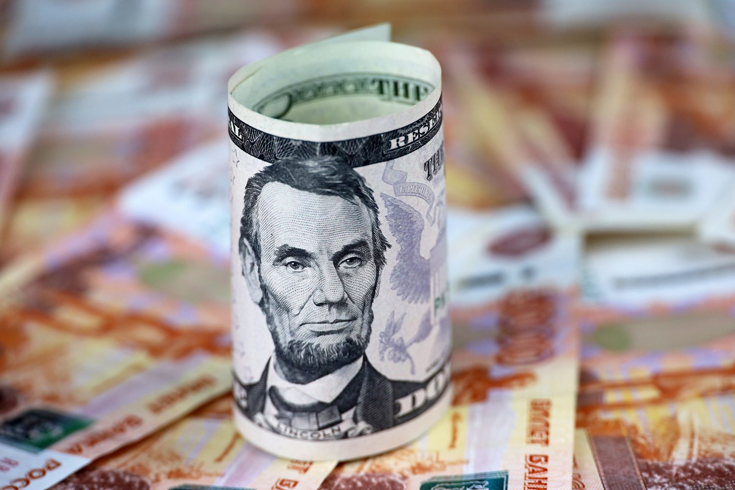 Un billete de dólar estadounidense sobre un lecho de billetes de rublo ruso dispersos.