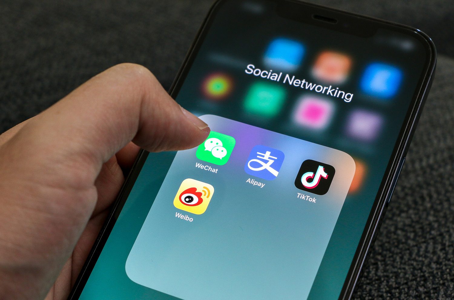 La mano de una persona sostiene un teléfono móvil y está a punto de lanzar una aplicación de redes sociales china, en la que se muestran los iconos de WeChat, Alipay, TikTok y Weibo.