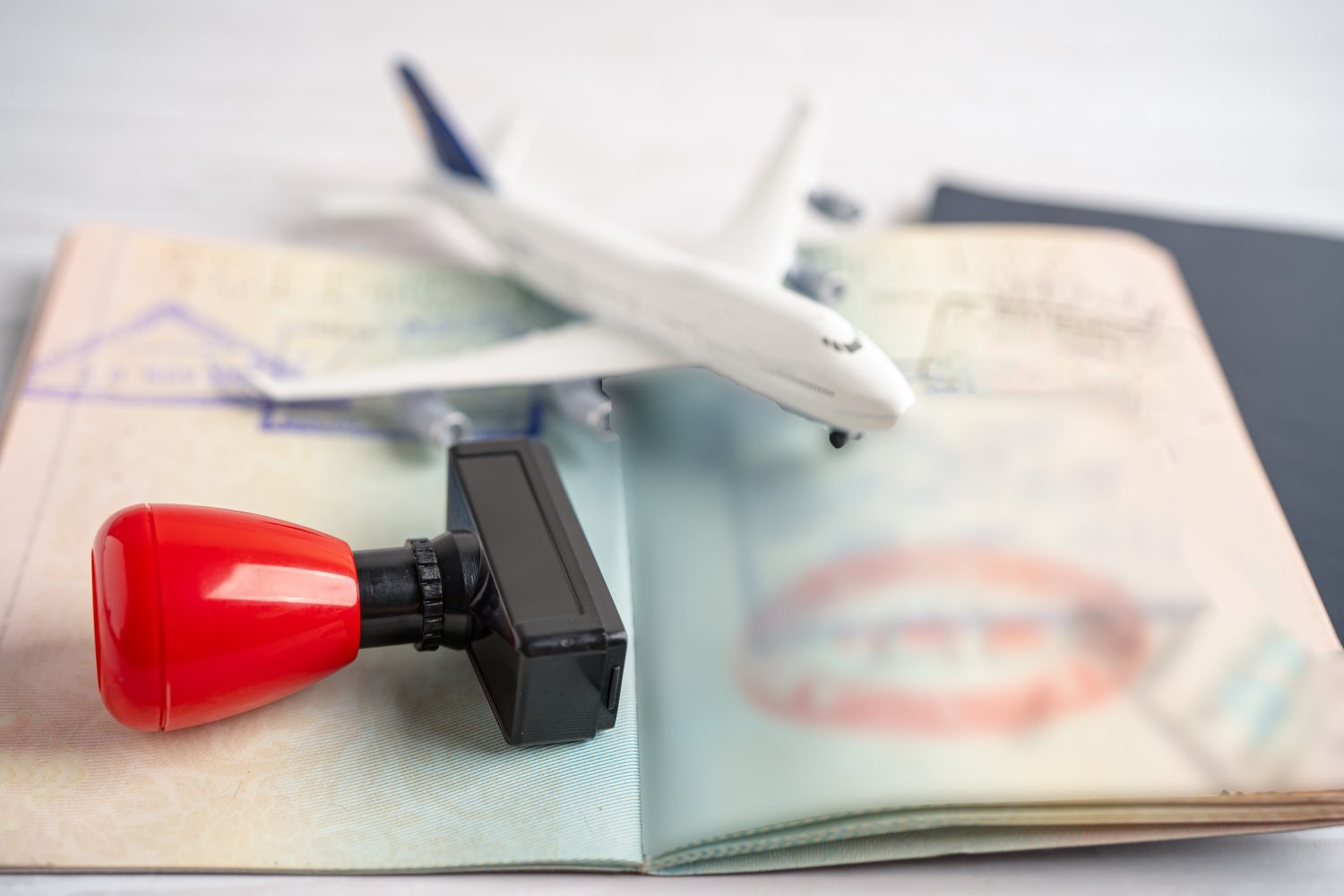 Un sello de visa y un pasaporte abierto, coronados por un pequeño modelo de avión.