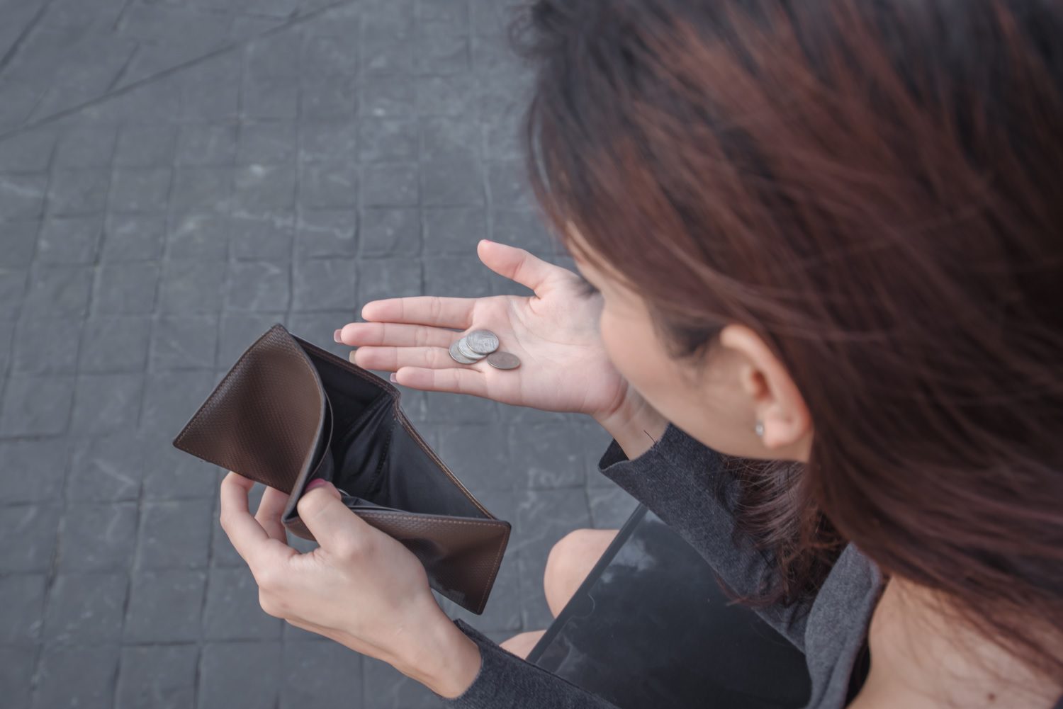 Una mujer sostiene algunas monedas en una mano y una billetera vacía en la otra.