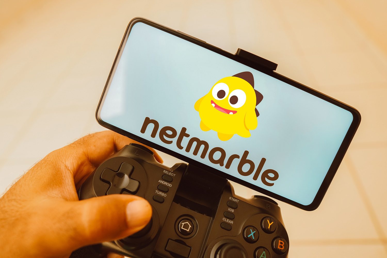Una persona sostiene un joystick conectado a un teléfono móvil con el logotipo de Netmarble en la pantalla del teléfono.